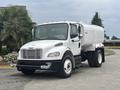 A 2006 Freightliner M2 106 water truck with a white body and large tank mounted on the back parked at an angle