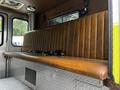 A brown leather bench seat in the interior of a 1995 Freightliner FLL086 with a diamond plate metal surface below
