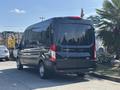 A black 2025 Ford Transit T-350 van is parked, showcasing its rear view with a sleek design and large windows
