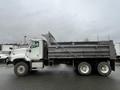 A 2003 International 5600i dump truck with a white cab and gray dump bed is shown in profile on a wet surface with a double rear axle