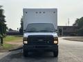 A 2008 Ford Econoline van is parked in front of a large white box truck with its front facing the camera and headlights illuminated