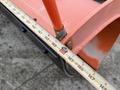 A close-up of a snowplow blade with an orange coating and a measuring tape indicating a width of approximately 14 inches