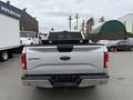 A rear view of a silver 2015 Ford F-150 with a Ford logo on the tailgate and a black bed cover