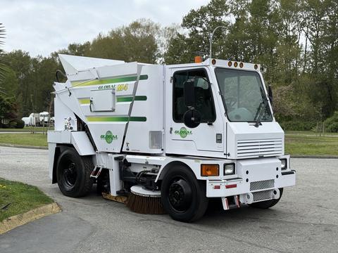 A white 2012 Global M4 street sweeper with green and yellow graphics featuring a front-mounted broom and a compact design for urban cleaning