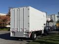 A white 2011 Freightliner M2 106 box truck with a closed rear door and silver chassis parked on a street