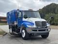 A blue and gray 2013 International DuraStar 4300 street sweeper with a rotating broom at the front and side mirrors