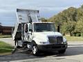 A 2012 International 4300 dump truck with a metallic dumping bed raised in the foreground