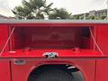 A red truck bed with an open storage compartment featuring a diamond plate top and chains supporting the interior sides