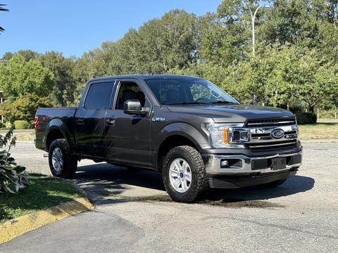 A 2018 Ford F-150 truck in dark gray with chrome accents and off-road tires parked at an angle with its front facing towards the viewer