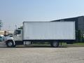A white 2012 Hino 338 box truck with a large cargo area and a flatbed in the rear is positioned sideways on a road