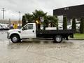 A white 2008 Ford F-350 flatbed truck with no bed cover and a small load is parked on a wet surface with palm plants on the bed