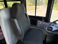 A black driver's seat with a padded backrest and armrest stands in a vehicle's cab next to a control panel featuring various buttons and switches