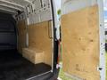 A 2022 Mercedes-Benz Sprinter van with its rear doors open revealing plywood panels and a wooden crate inside the cargo area