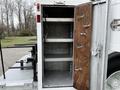 An open storage compartment of a 2005 Freightliner M2 106 with three empty shelves and a wooden door on one side