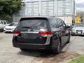 A 2014 Honda Odyssey minivan in black parked with the rear facing the viewer showing the taillights and Honda logo