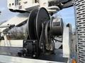 A close-up of a winch assembly mounted on a 2013 International Durastar 4300 featuring a black spool a control box and hydraulic components