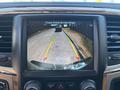 A rearview camera display shows a 2015 RAM 1500 backing up with guidelines indicating distance to nearby vehicles on a road