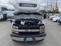 A 2020 Chevrolet Express with its hood raised displaying the engine compartment and an illuminated "EMERGENCY" sign