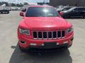 A red 2015 Jeep Grand Cherokee facing forward with chrome accents on the grille and hood and a black front bumper