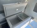 A white chest freezer with a lid open revealing two compartments one empty and one with a wire basket inside