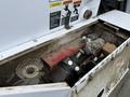 A compartment of a 2012 Global M4 revealing tools and parts including a red base, a pump, and a circular filter among dirt and debris