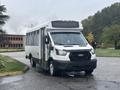 A white 2021 Ford Transit-350 with a large passenger compartment and dual sliding doors is parked at an angle on a wet surface