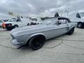 A silver 1968 Ford Mustang two-door convertible with a black soft top and black wheels parked on a paved surface