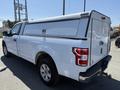 White 2019 Ford F-150 pickup truck with a camper shell on the bed and a tow hitch visible at the rear