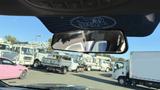 A 2016 Ford F-150 viewed from inside another vehicle with a Ford logo visible on the rearview mirror
