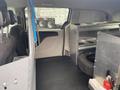 Interior of a 2014 RAM Cargo Van featuring metal storage shelving and a tire in the cargo area with a black rubber floor liner and a blue tool on the side