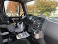 Interior of a 2013 Freightliner 114SD featuring a driver’s seat steering wheel gear shifter and control panels designed for heavy-duty vehicle operation