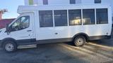 A white 2021 Ford Transit van with large windows and a side entry door is parked on gravel ground