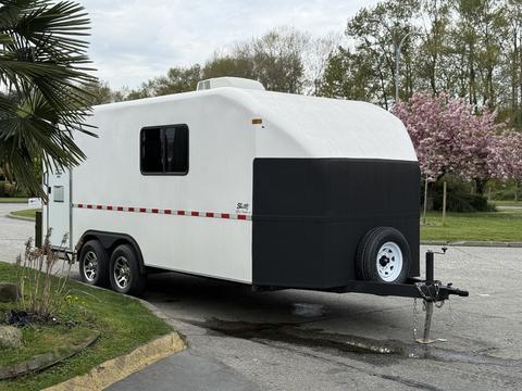 A white and black 2025 Shuttle Office trailer with two axles and a front hitch, featuring a rounded roof and a small vent on top