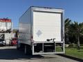 A white 2017 Freightliner M2 106 box truck with a closed rear door and a diamond-shaped reflective sign on the back