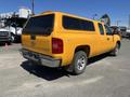 A yellow 2013 Chevrolet Silverado 1500 pickup truck with a camper shell and chrome accents parked with a visible rear view and the Chevrolet logo on the tailgate