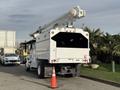 A white 2011 International 4300 bucket truck with an elevated boom and a rear compartment, positioned in a parking area with a traffic cone nearby