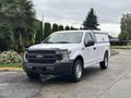 A white 2020 Ford F-150 with a truck cap parked on a street surrounded by greenery