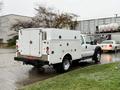 A 2015 Ford F-450 truck with a white service body and closed compartments is parked with its rear facing the viewer