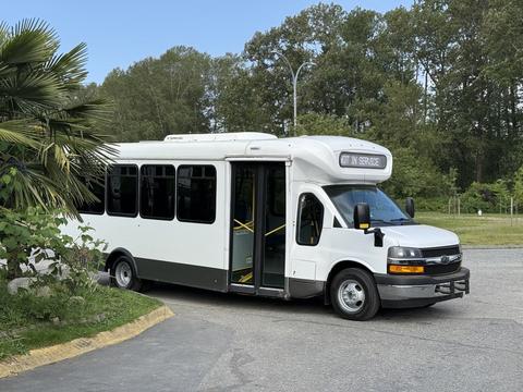 A white 2020 Chevrolet Express shuttle bus with an open side door and a sign displaying "IN SERVICE"