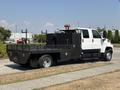 A 2005 GMC C7500 Topkick truck with a flatbed, black storage compartments, and an orange light on top parked on a grassy area