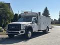 A white 2011 Ford F-550 utility truck with a service body and utility compartments parked on a street