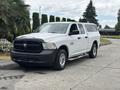A white 2013 RAM 1500 pickup truck with a black front grille and a camper shell in the bed parked on a road