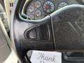 Close-up of a black steering wheel with buttons on the left side and a visible dashboard with various gauges in the background