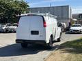 A white 2019 GMC Savana van with a ladder rack on top parked in a lot