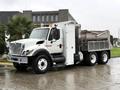 A 2011 International 7500 truck with a white cab and a gray dump bed parked on a wet surface