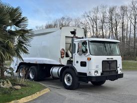 A white 2010 Autocar Xpeditor garbage truck with a large rear compactor and front cabin, featuring a single door on the driver side and various utility equipment mounted on the chassis