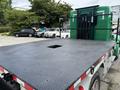 A green 2013 Kenworth T370 truck with a flatbed featuring a rectangular hole at the center of the bed surface