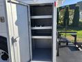 An open compartment of a 2005 Freightliner M2 106 showing three empty gray shelves with a door on the left side