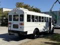 A white 2013 International CE300 school bus with a rounded back and large windows is parked with its rear facing the viewer