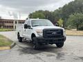 A white 2013 Ford F-250 SD pickup truck with a black front grille and black wheels parked on a street